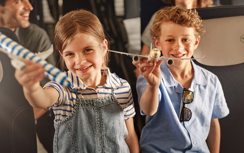 Allein oder in Begleitung reisende Kinder Mädchen und Junge stehend im Flugzeug mit einem Miniflugzeug in der Hand