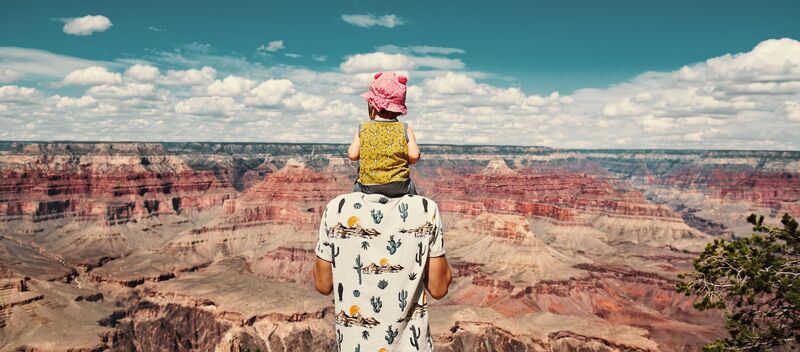 Familienabenteuer USA Ein Mann steht über dem Grand Canyon, sein kleines Kind hat er auf den Schultern