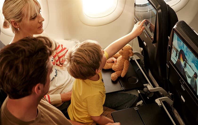 Eltern im Flieger mit Kind auf dem Schoß, schauen einen Film im Inseat Enterrtainment