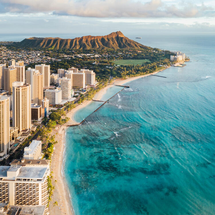 Atemberaubender Blick auf Waikiki Beach und Diamond Head Crater bei Sonnenaufgang, mit klarem blauen Wasser und Hochhäusern entlang der Küste