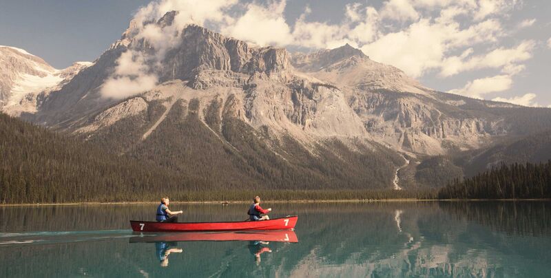 Ein rotes Kanu mit einer Familie liegt auf einem türkisblauen See, im Hintegrund die Rocky Mountains