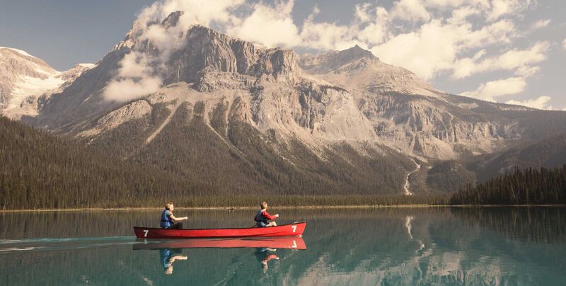 Abenteuerurlaub in Kanada Ein rotes Kanu mit einer Familie liegt auf einem türkisblauen See, im Hintegrund die Rocky Mountains