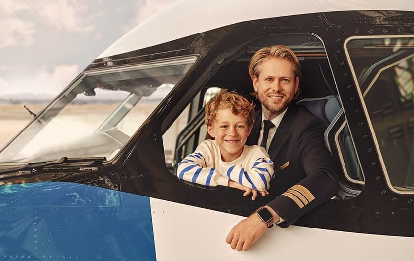 Stellenangebote Cockpit Kapitän mit kleinem Jungen im Cockpit, die aus dem geöffenten Fenster schauen.
