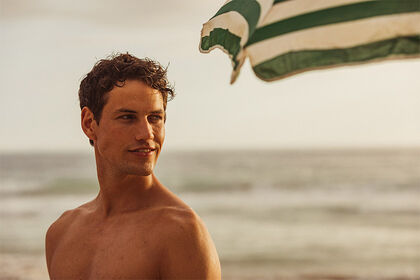 Mann am Strand mit grün gestreiftem Sonnenschirm 