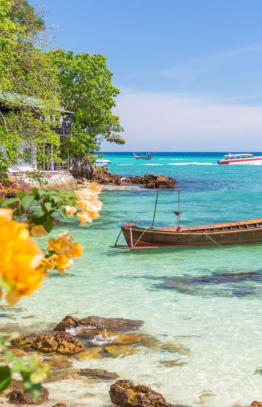 Ein Fischerboot am Strand von Ko Phi Phi mit blühenden Pflanzen und einem Meer aus Steinen