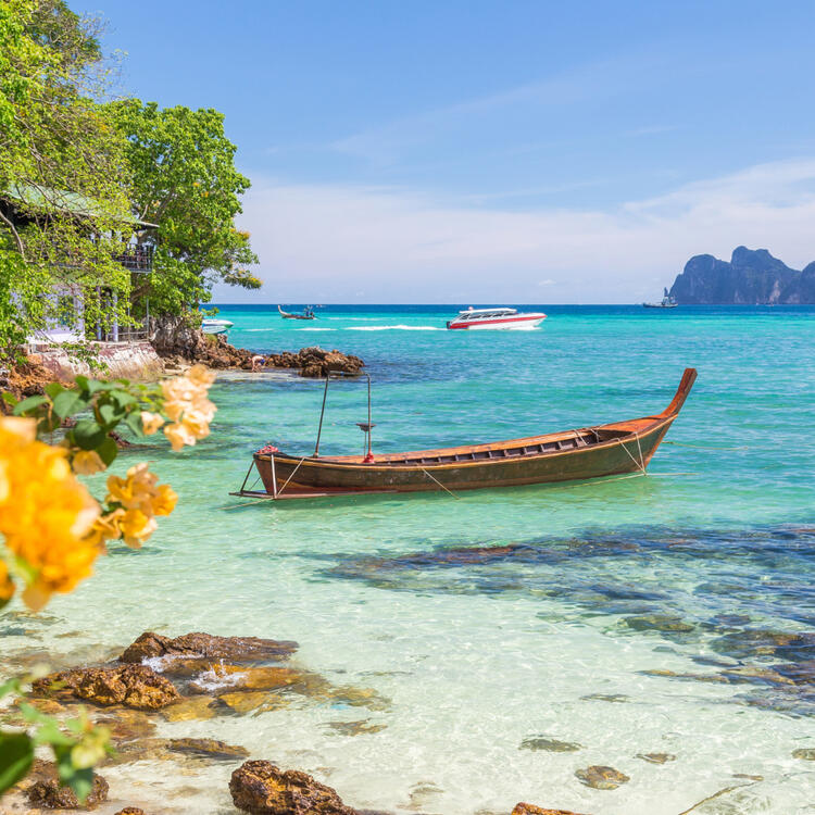 Kristallklares türkisfarbenes Wasser an einem sonnigen Strand auf den Ko Phi Phi Inseln nahe Phuket, Thailand, mit einem traditionellen Langboot 