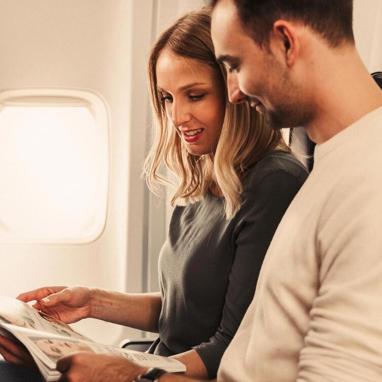Ein Mann und eine Frau lesen gemeinsam ein Magazin im Flugzeug.