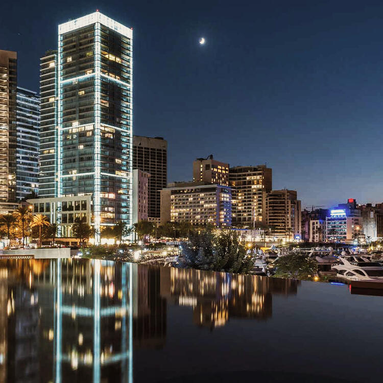 Die funkelnde Skyline der Zaitunay-Bucht bei Nacht, mit Wolkenkratzern, die sich in der glatten Wasseroberfälche des Jachthafens von Beirut spiegeln.