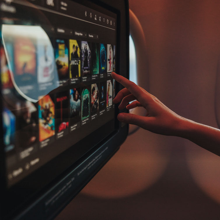 Eine Person navigiert auf dem Bildschirm am Sitz des Flugzeugs durch das Unterhaltungsprogramm