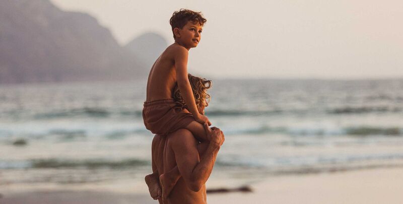 Ein Vater steht mit seinem Sohn auf den Schultern am Meer