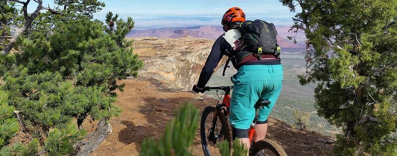 Rücken eines Moutainbikers fährt einen Trail auf einem Berg mit Blick auf Moab, Utahau