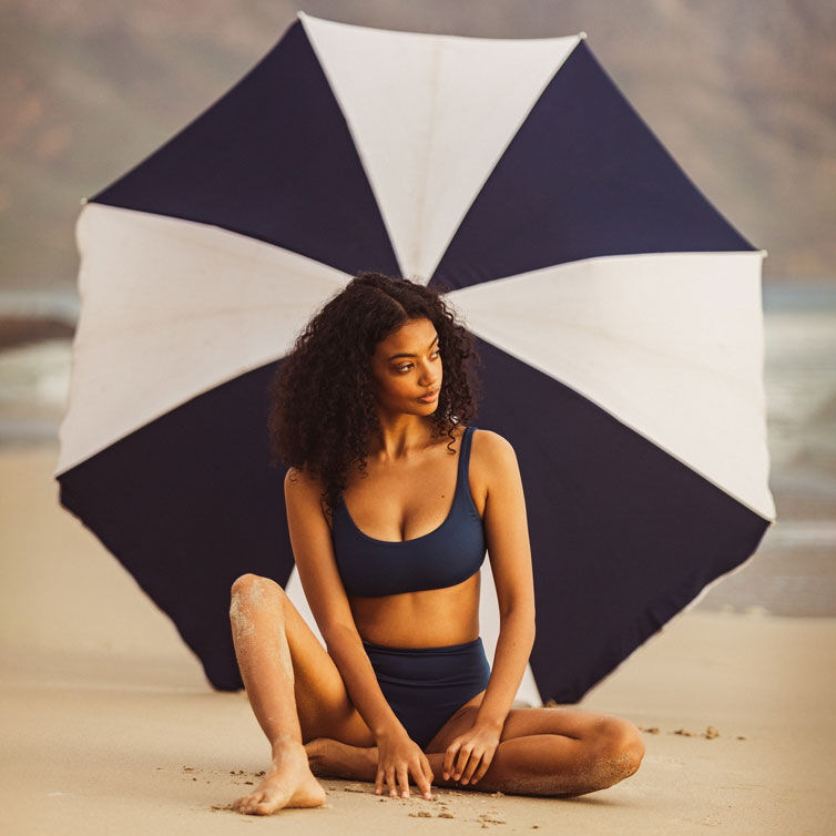 Eine Frau sitzt gut geschützt unter einem Sonnenschirm am Strand