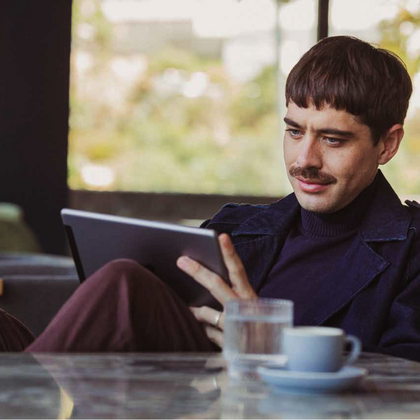 Ein Mann sitzt mit Laptop und Kaffee in einer Lounge.