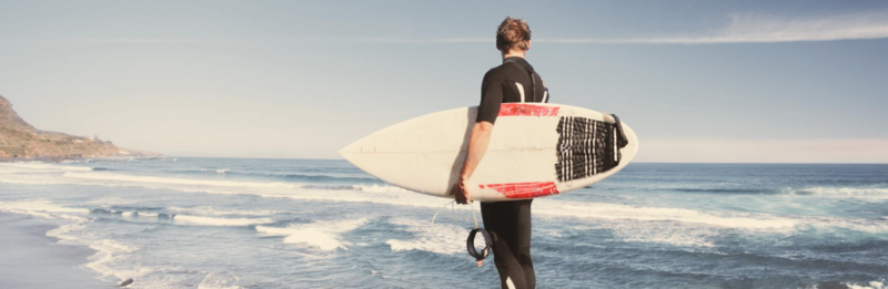 Ein Surfer steht mit seinem Surfboard in der Brandung