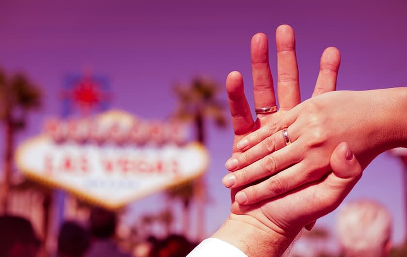 Brautpaar zeigt seine Eheringe vor dem Las Vegas Schild