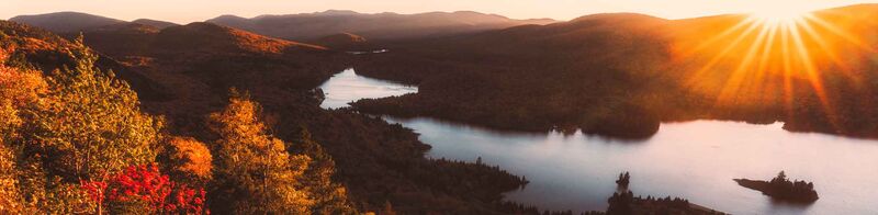 Eine Naturszene in Kanada mit der strahlenden Sonne, einem See und bunten Laubbäumen