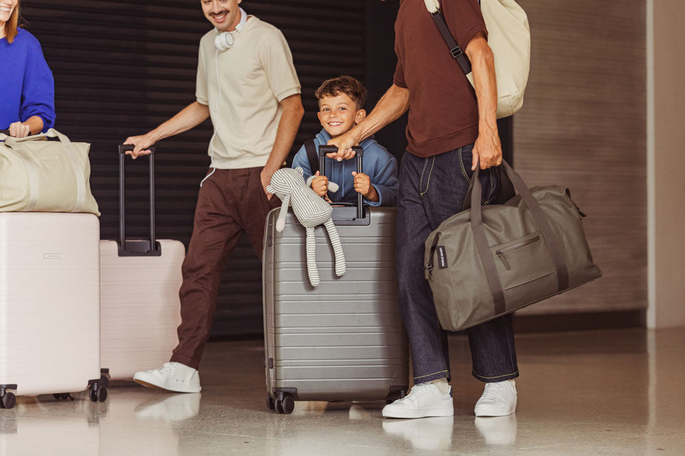 Ein kleiner Junge durchquert mit seiner Familie und vielen Koffern einen Flughafen; sein Stoffaffee liegt bei ihm im Arm