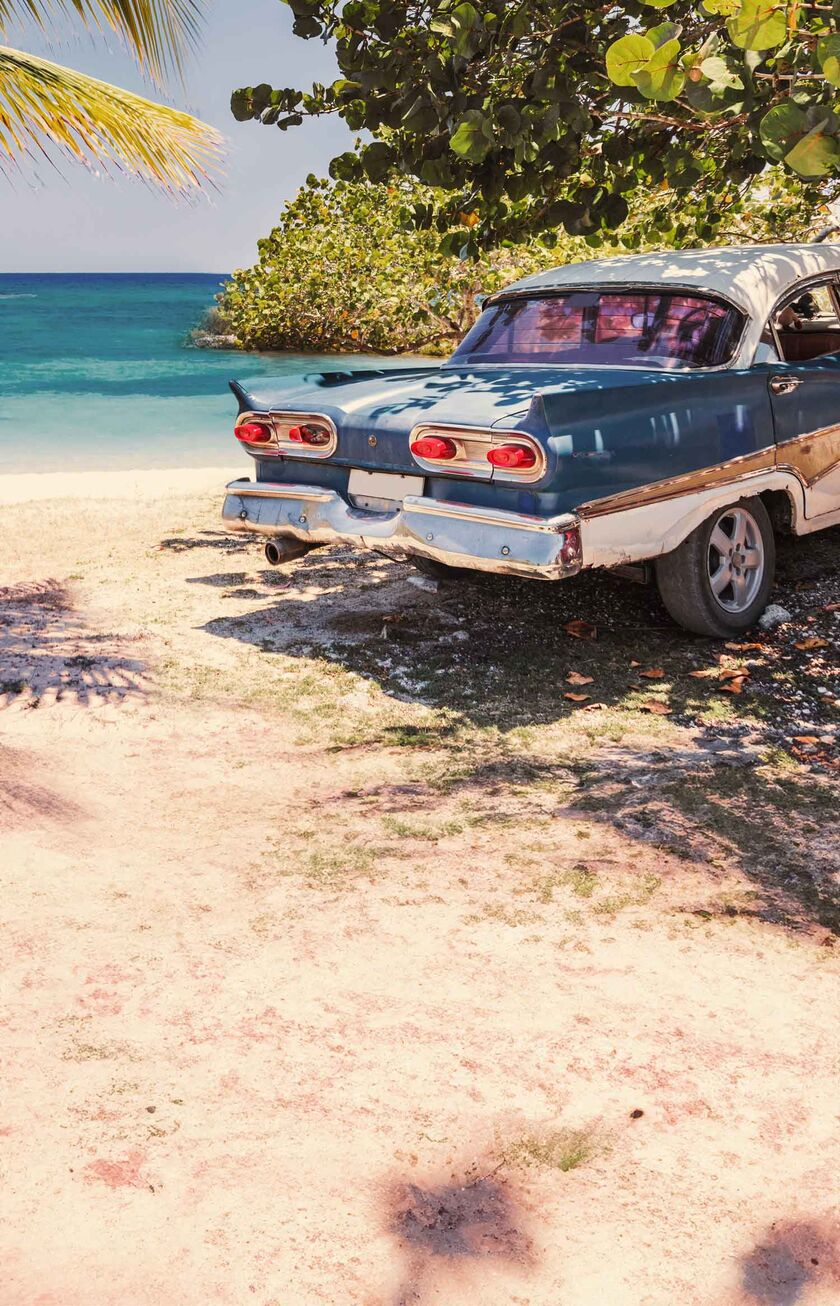 Ein Oldtimer steht am Strand unter Palmen