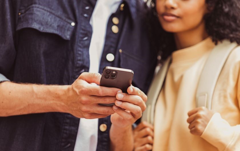 Man sieht 2 Oberkörper eines Mannes und einer Frau, die auf ein mobiles Endgerät schauen. 