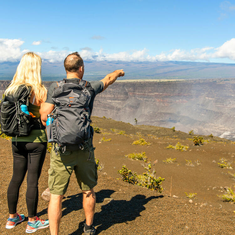 Ein Paar betrachtet die ausgedehnte Landschaft des Hawaiʻi Volcanoes National Park, sichtbar sind weite Lavafelder und üppige Vegetation