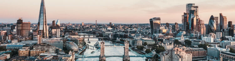 Luftaufnahme von London bei Sonnenuntergang mit der Tower Bridge, der Themse und modernen Hochhäusern.