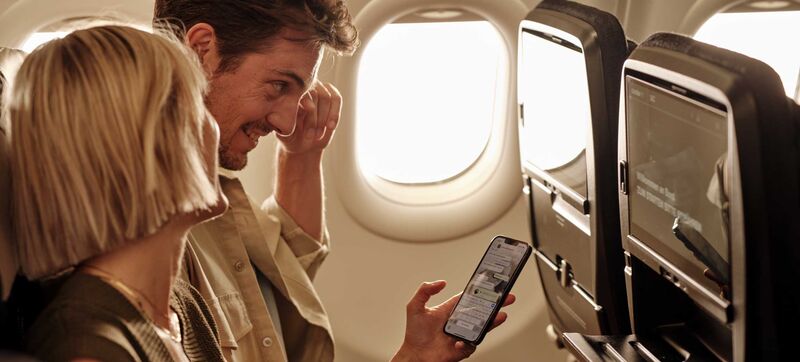 WLAN an Bord Ein Paar sitzt an Bord eines Flugzeugs und liest gemeinsam auf dem Smartphone Chatnachrichten