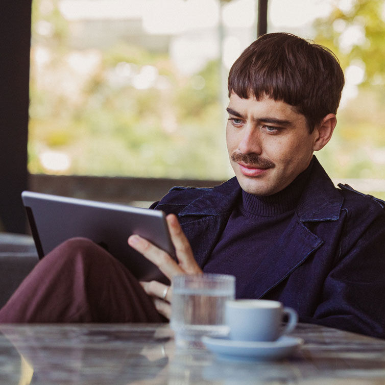 Ein Mann liest auf seinem Tablet eine Zeitschrift und trinkt dabei Kaffee