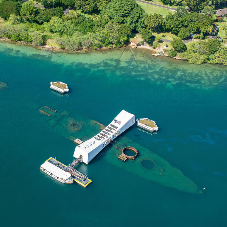 Luftaufnahme des Pearl Harbor mit dem USS Arizona Memorial und weiteren historischen Schiffswracks in klarem blauem Wasser.