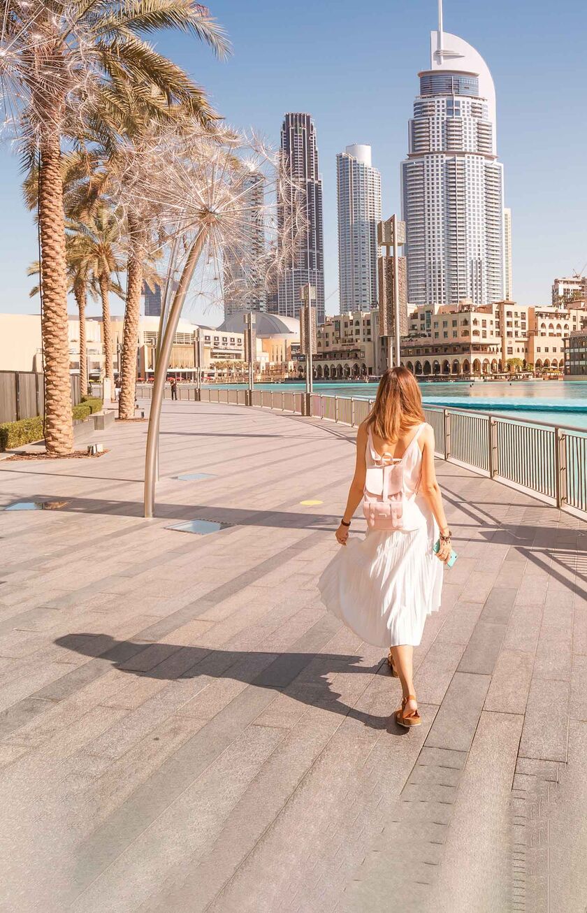 Eine Frau läuft am Wasser in Dubai entlang auf die Stadt zu