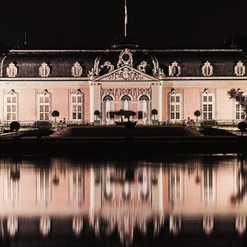 Schloss Benrath spiegelt sich im Wasser bei Nacht.
