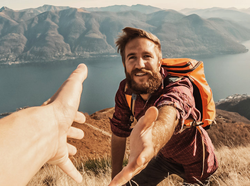 Ein Wanderer in einer Fjordlandschaft reicht einem Mitwanderer die Hand Ein Wanderer in einer Fjordlandschaft reicht einem Mitwanderer die Hand