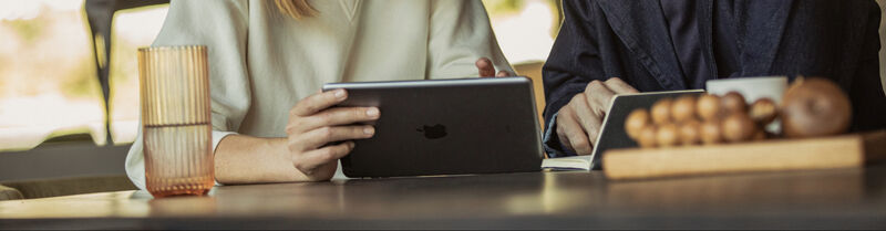two people sitting at a table clicking at an ipad