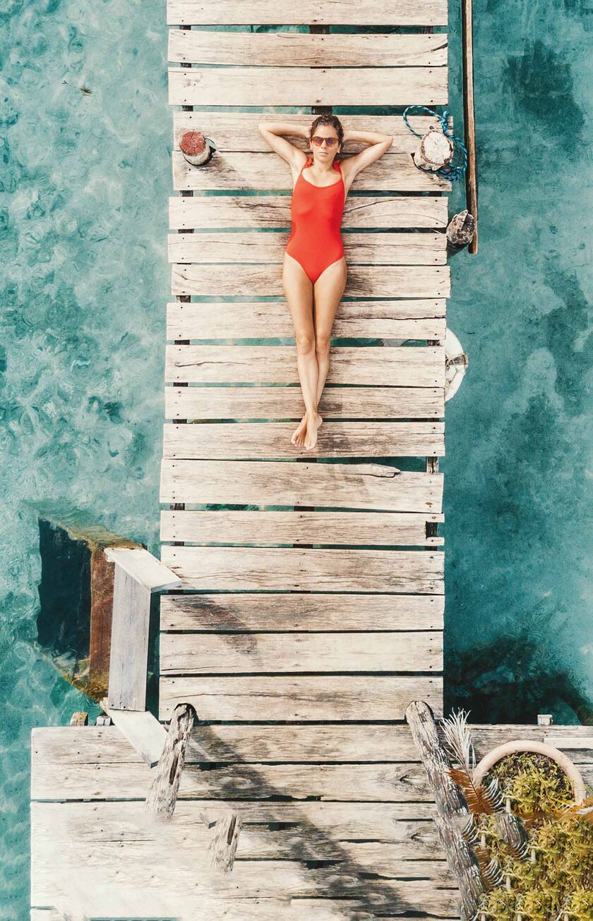 Una mujer en traje de baño rojo descansa en un embarcadero, con el mar turquesa de Cancún bajo sus pies.