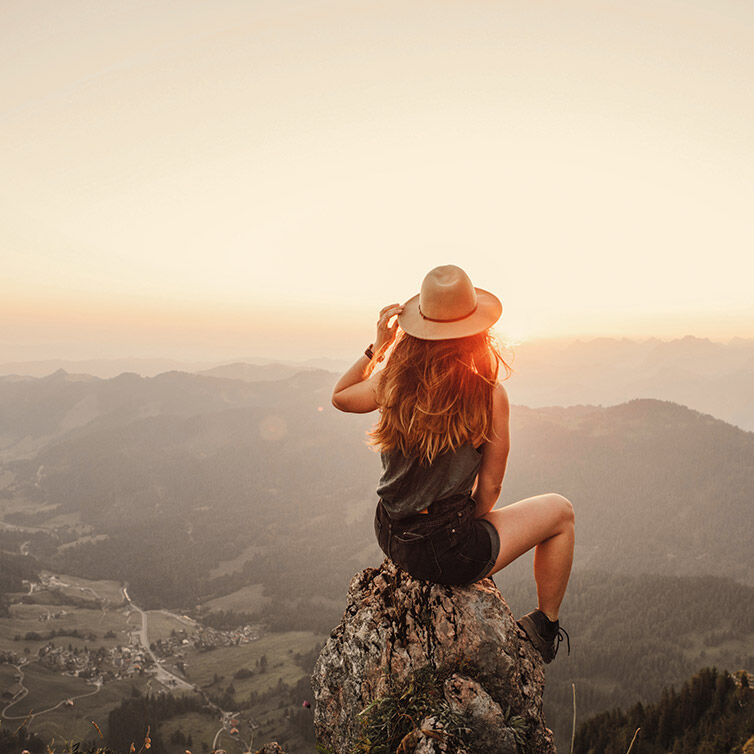 Mujer sentada en una piedra en las montañas de Suiza, mirando el horizonte al atardecer