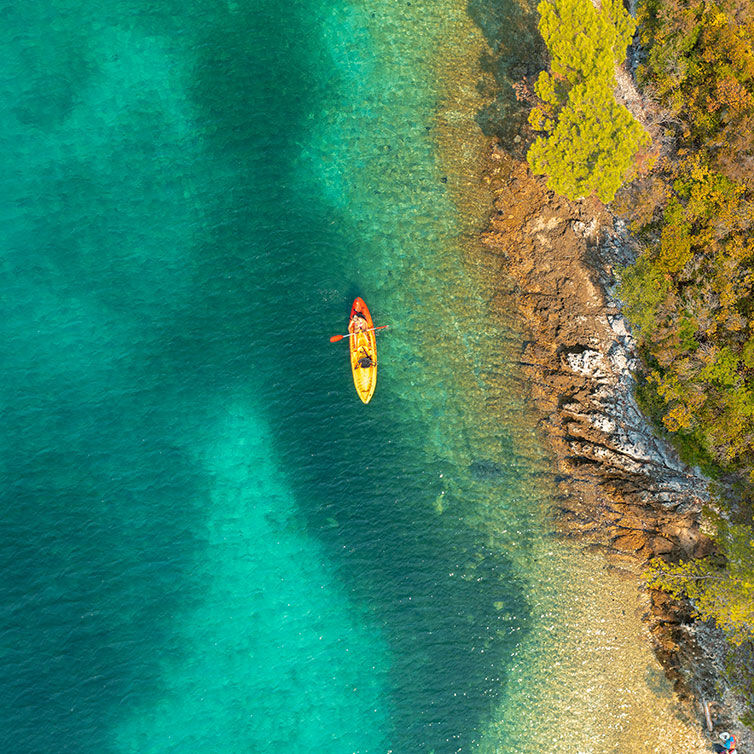 Vista aérea de la costa croata con sus aguas turquesas, un kajak navega cerca de la costa