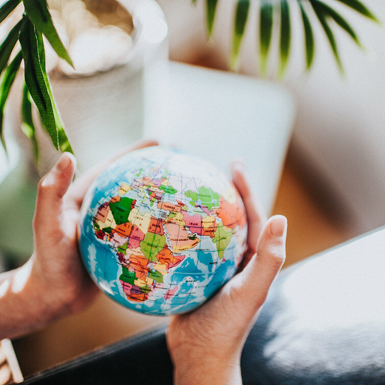 The hands are holding a ball of the world, showing mainly the continents of Europe and Africa.
