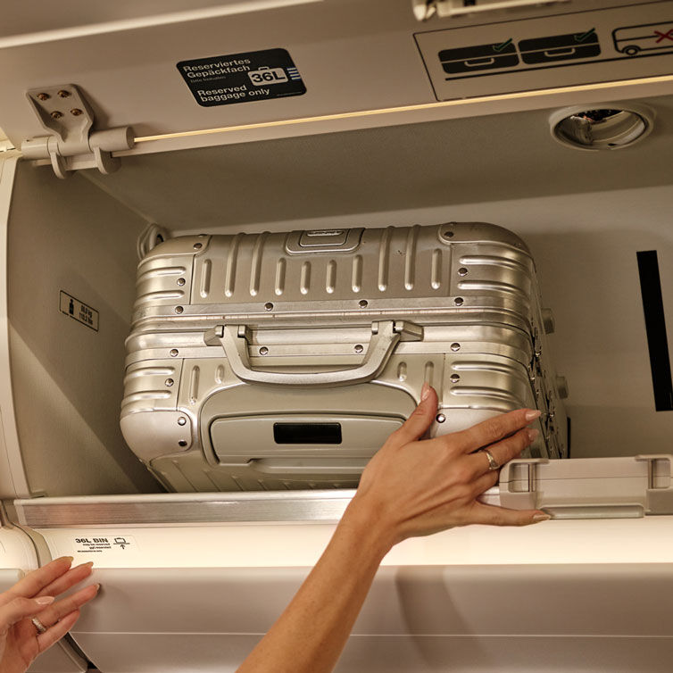 Mujer colocando una maleta color plata en el compartimento de equipaje de un avión