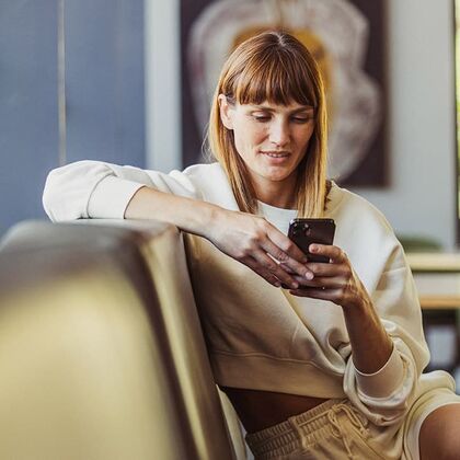 Portal de recibos electrónicos Mujer sentada un un sofá y consultando su dispositivo móvil.