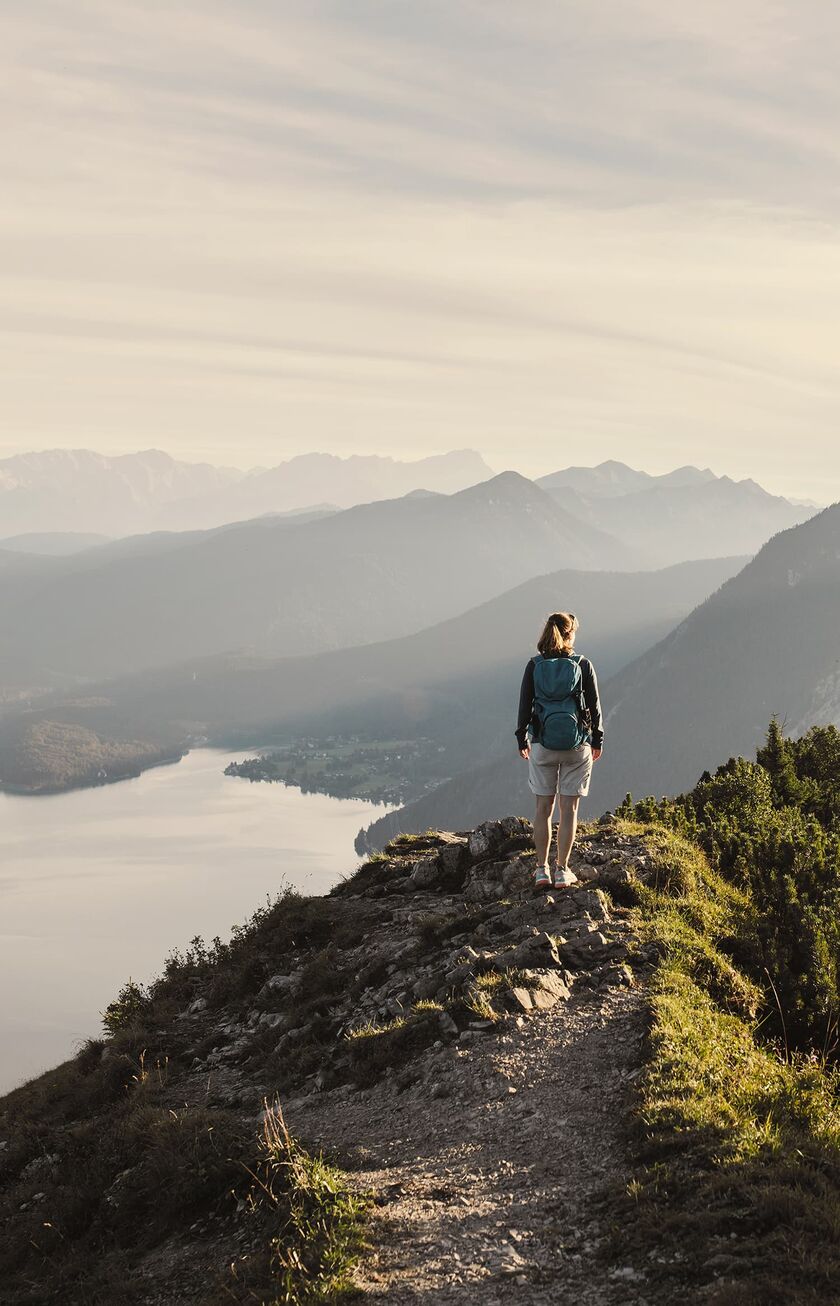 Una mujer de pie en una montaña, un lago bajo ella y los Alpes al fondo