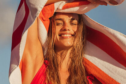Mujer sonriente en la playa con una toalla de rayas rojas.