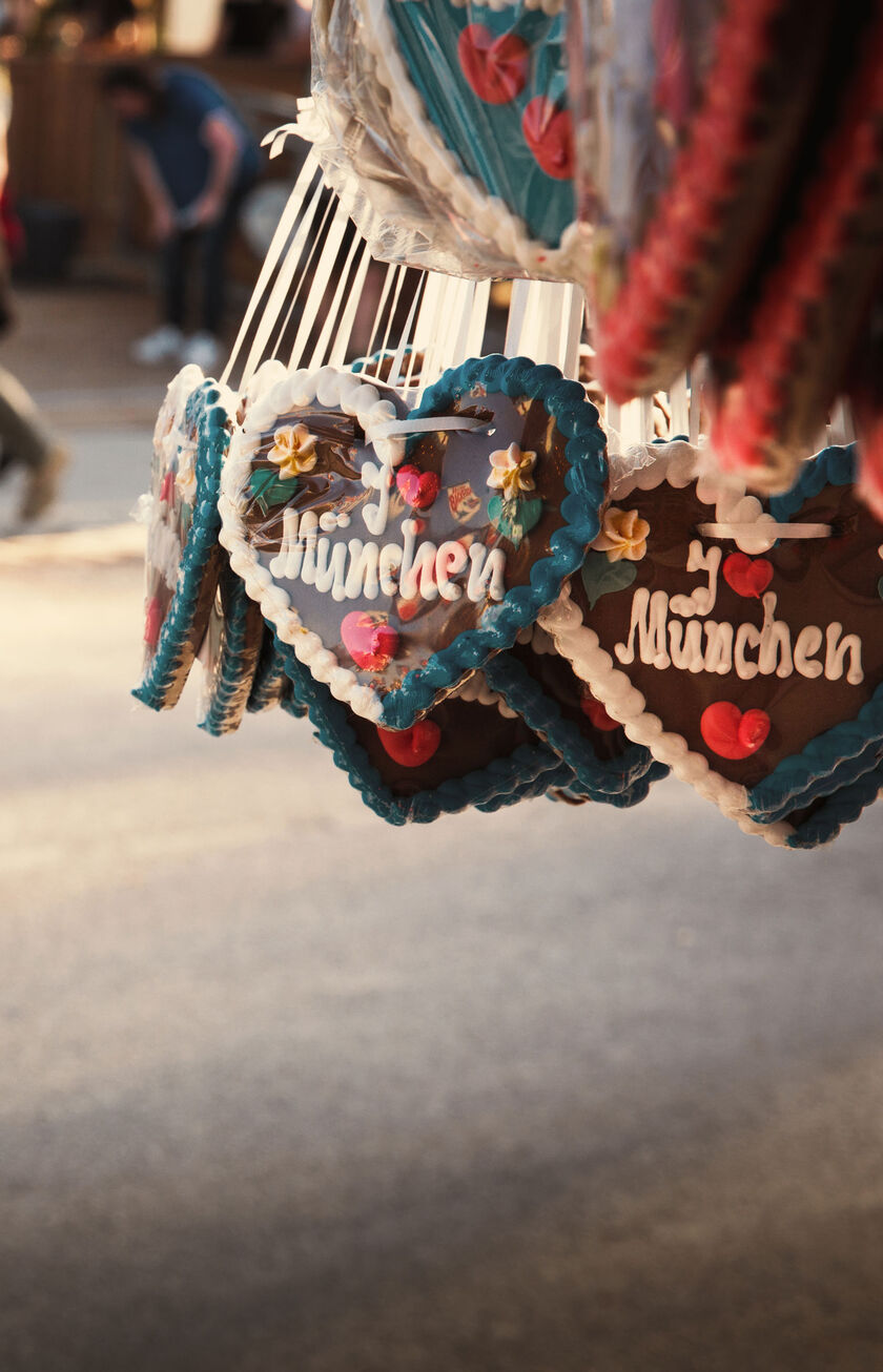 Una escena de la Oktoberfest con gente en trajes tradicionales, corazones de pan de jengibre tradicionales en primer plano.