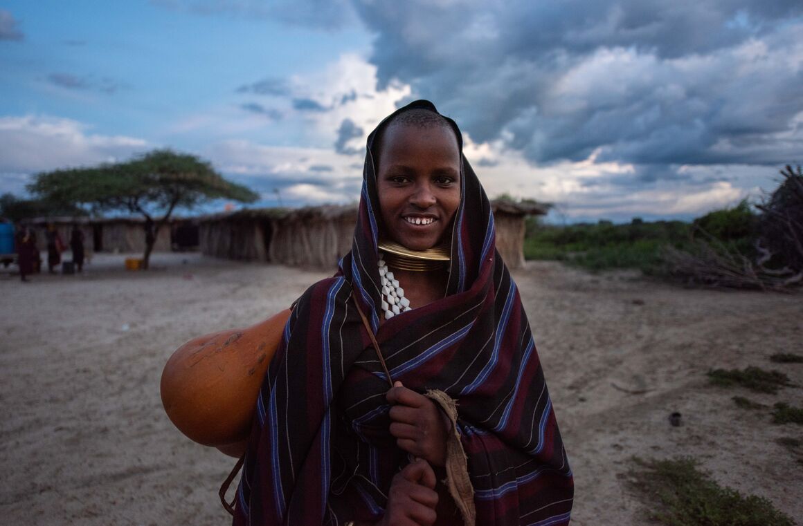A woman in traditional dress in front of a tree, surrounded by steppe