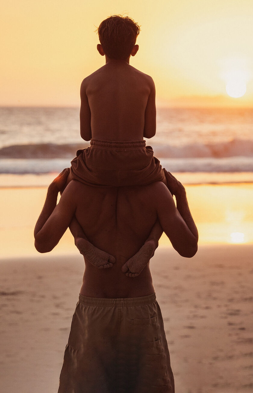 A man and his son are overlooking the sea at sunset