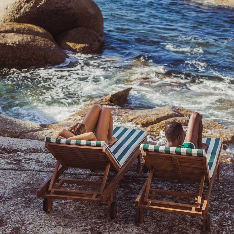 A couple lounges on two striped beach chairs by the sea.