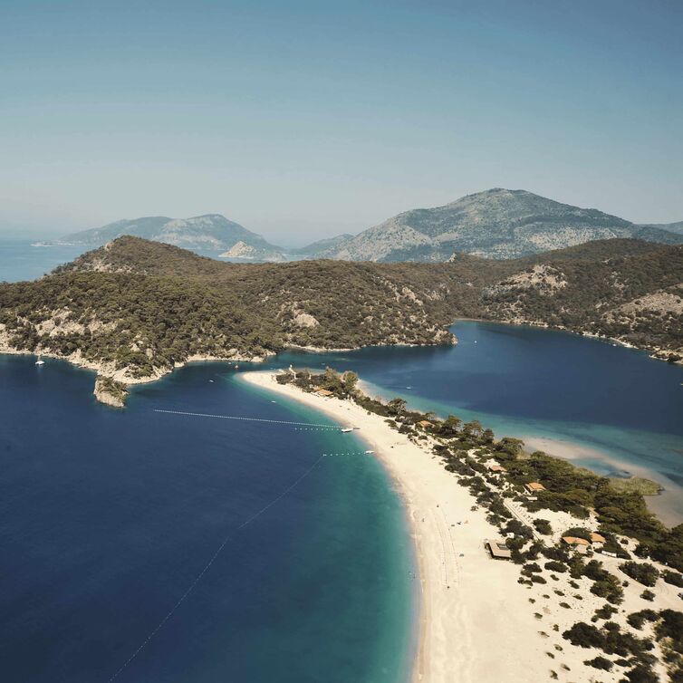 A coastline in Turkey with a white sandy beach and deep blue sea, surrounded by nature
