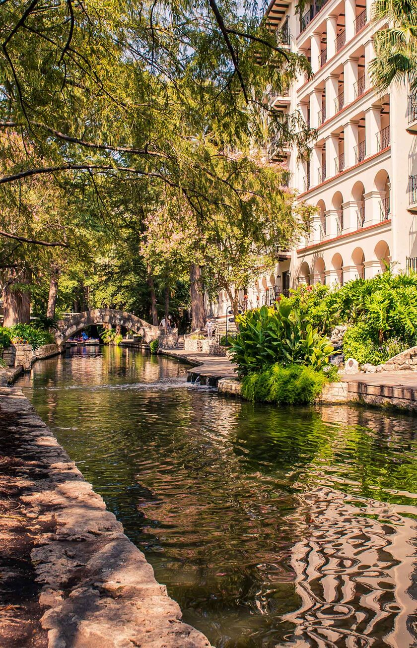 A serene river lined in San Antonio, Texas, with lush greenery and historic buildings under a clear sky
