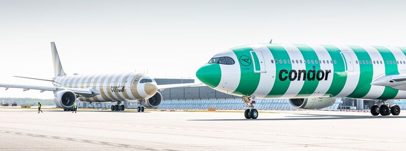Green-striped Condor A330neo at boarding gate with fuel truck, service lift, and clear blue sky overhead.Green-striped Condor A330neo at boarding gate with fuel truck, service lift, and clear blue sky overhead.