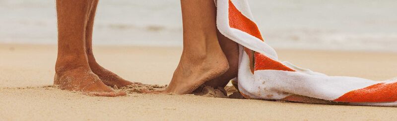 A detail: two feet in the sand, next to a red and white striped towel
