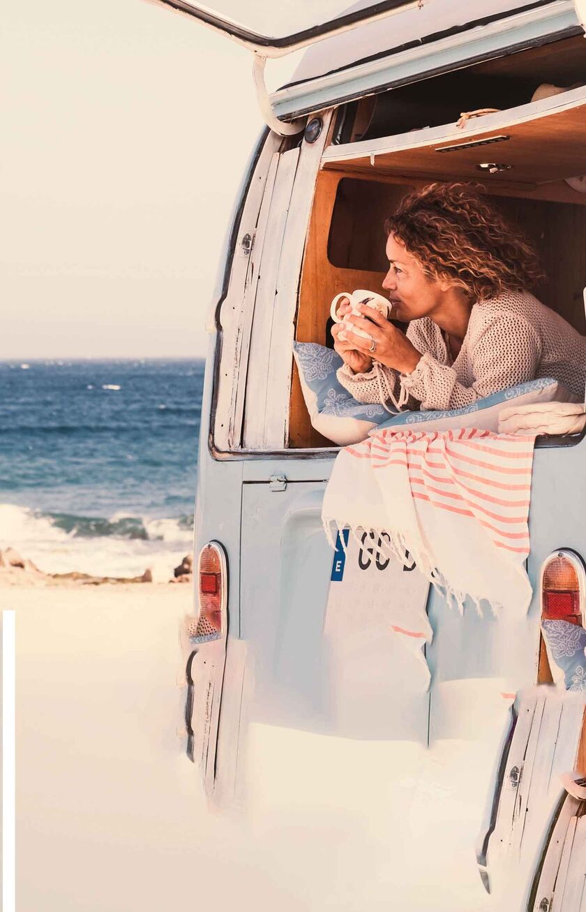 A woman looks out to sea from her camper, a cup of coffee in her hand