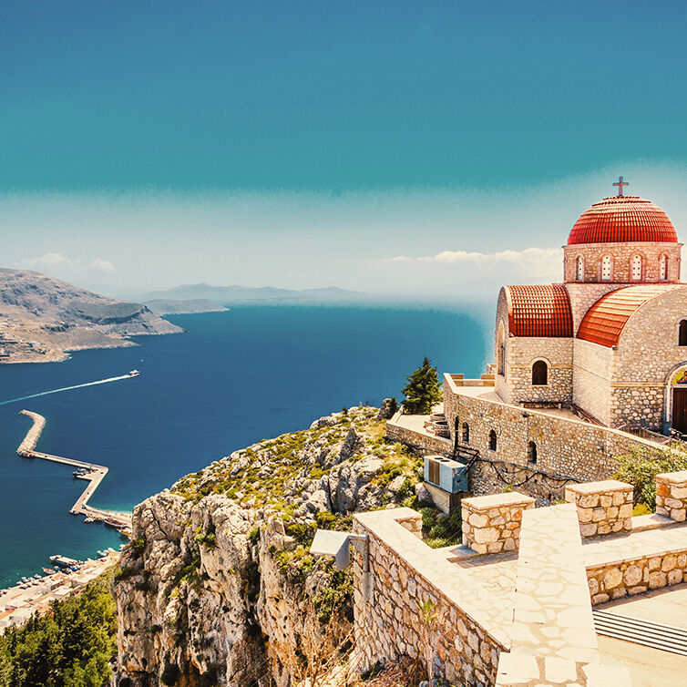 A dome roofed cathedral on top of a cliff on a Greek island; below is the blue sea